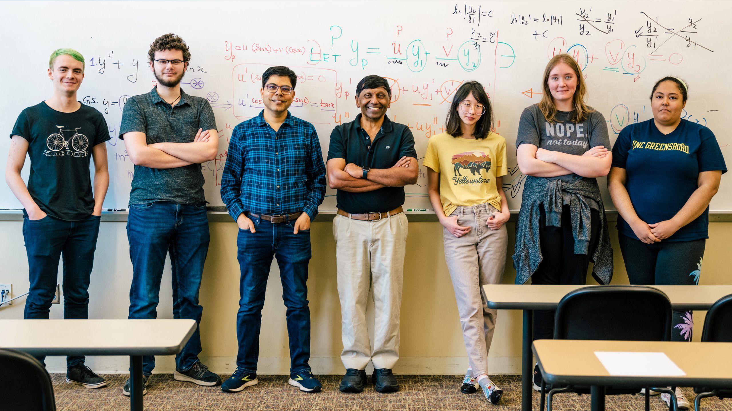 Dr. Shivaji stands with his students in front of a white board covered in math equations.